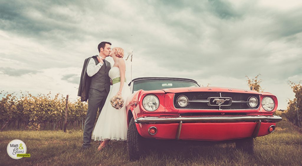 Hochzeitspaar küssend vor rotem Mustang